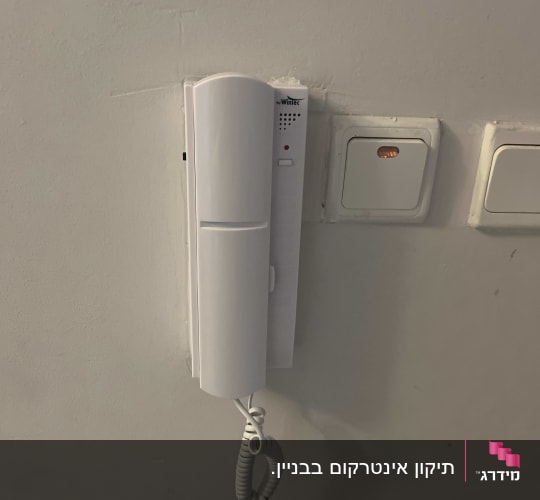 אינטרקום לבן מותקן על קיר עם כבל טלפון